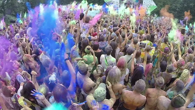 Happy crowd throws paint powder in air, festival atmosphere