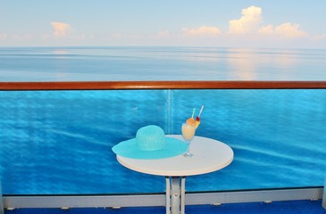 Pina Colada and a summer hat laying on a table with the ocean in