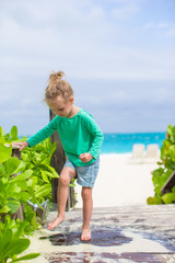 Little cute girl washes out the sand from her feet on tropical