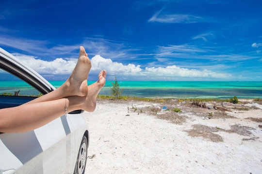 Female barefoot from the window of a car on background tropical