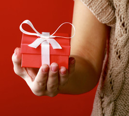 Female hand holding gift box isolated on red