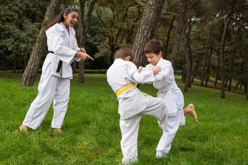 Two kids practicing judo outdoors in a park under the supervisio - 72182971