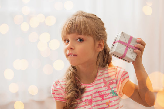 Cute little girl holding a gart box at home. Holiday lights arou