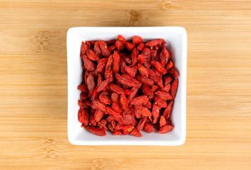Macro of dehydrated red goji berries in white bowl against woode