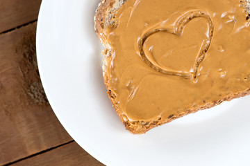 Peanut butter toast with heart shape on white against wooden boa