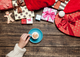 Female holding cup of coffee on wooden table near christmas gift