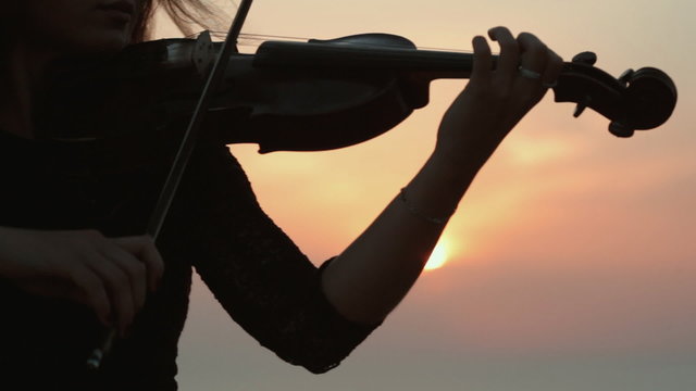 Beautiful girl playing the violin while the sun sets in the sea