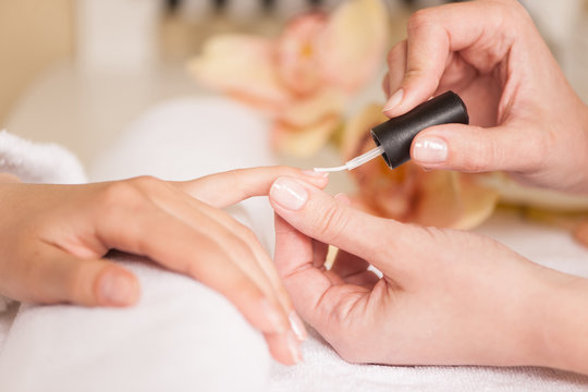 Woman in nail salon receiving manicure by beautician.