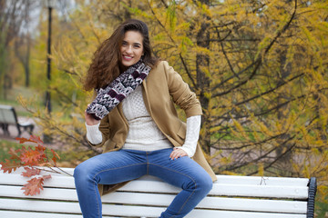 Naklejka na ściany i meble Beautiful woman sitting on a bench in autumn park