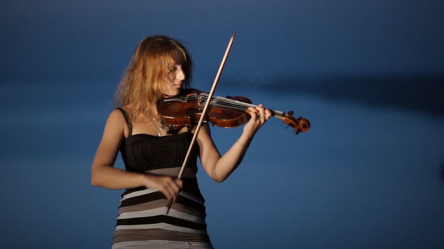 Talented girl playing the violin standing on a cliff next to the