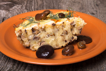 potato casserole with salted mushrooms in a clay plate on old wo