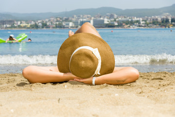 Fototapeta na wymiar Woman in a hat lying on the sandy beach
