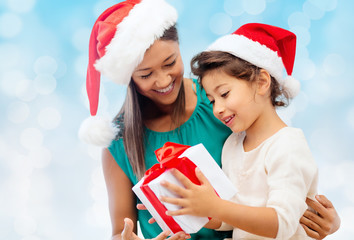 happy mother and girl in santa hats with gift box