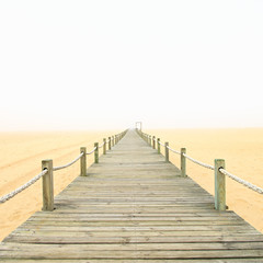 Obraz premium Wooden footbridge on a foggy sand beach background. Portugal.