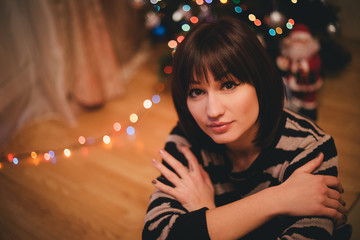 Pretty young woman near christmas tree in her cozy room