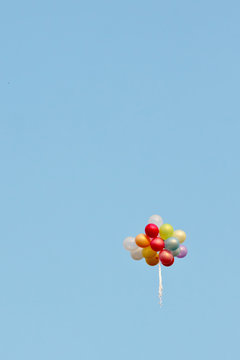 A bunch of painted balloons in a blue sky flying away