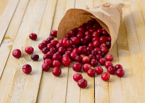 Cranberries in paper bag on yellow wooden background