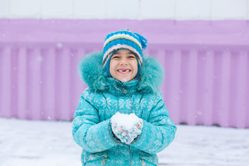 Happy kid girl child outdoors in winter playing holding snow