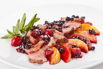 Slices of fried meat on a plate with fruit and berries.