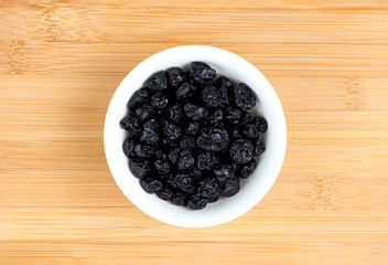 Dehydrated blueberries in bowl against wooden board