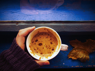 Hand in winter sweater holding a cup of coffee near the window