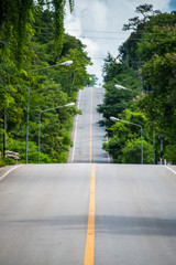 The beautiful long road cutting through the forest in the countryside of Thailand.