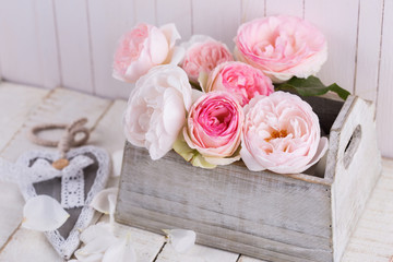 Fresh roses in box on white wooden background.