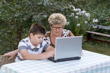 Granny with a grandson behind the laptop outdoors