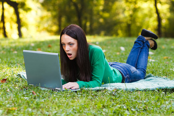 Surprised woman using laptop in park