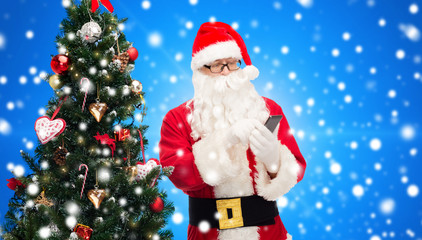 santa claus with smartphone and christmas tree