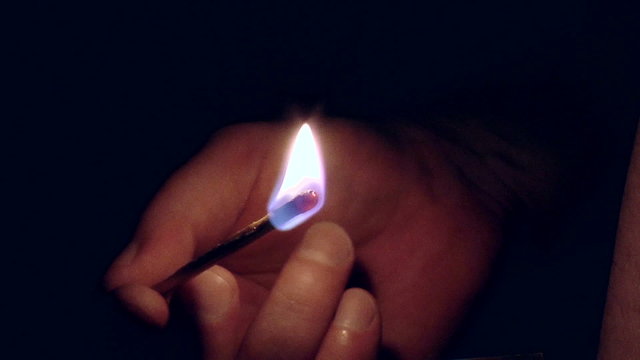 Hand holding burning match stick on black background
