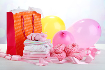 Baby clothes and gift bag on bright background