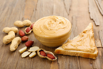 Creamy peanut butter in bowl on wooden table, close-up