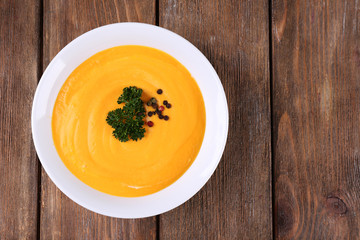 Pumpkin soup in white plate on wooden background
