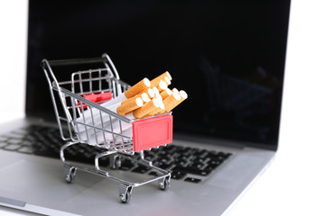 Shopping cart with cigarettes on laptop isolated on white