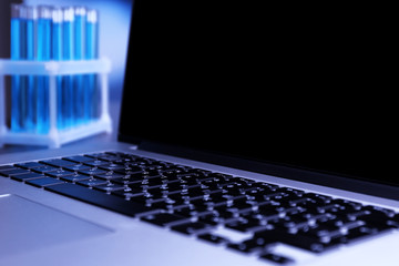 Laptop with test tubes in a laboratory on blue background