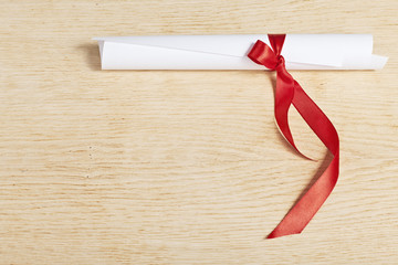 Scroll of paper with a red ribbon on a wooden surface.