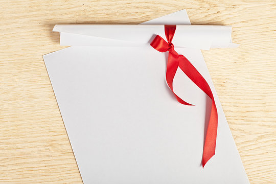 Scroll of paper with a red ribbon on a wooden surface.