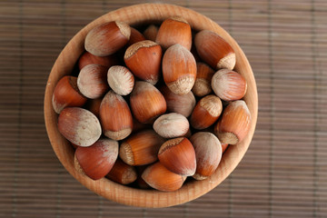 Hazelnuts in wooden bowl on bamboo mat background