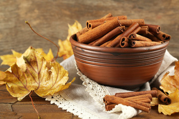 Cinnamon sticks in bowl with yellow leaves on wooden background