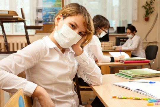 School Children In Medical Face Mask Are Learning In The Half Empty Classroom During Epidemic Of Flu.