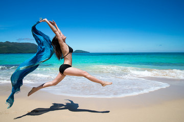 Fototapeta na wymiar Young girl jumping with waving blue scarf tropical beach