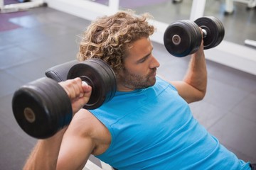 Fototapeta na wymiar Side view of man exercising with dumbbells in gym