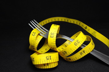 Measuring tape and fork on black background. Diet concept.