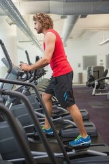 Side view of man working out on x-trainer in gym