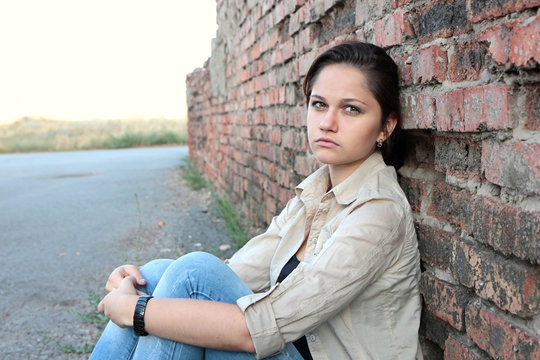 Sad young girl sitting against a brick wall