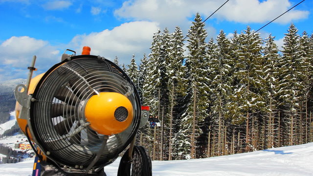 snow gun closeup, behind them people moving on hoist in mountain