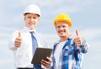 smiling builders in hardhats with tablet pc