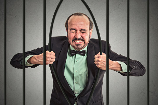 middle aged stressed businessman bending bars of his prison