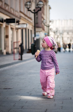 A little cute girl walking along the street with an ice-cream
